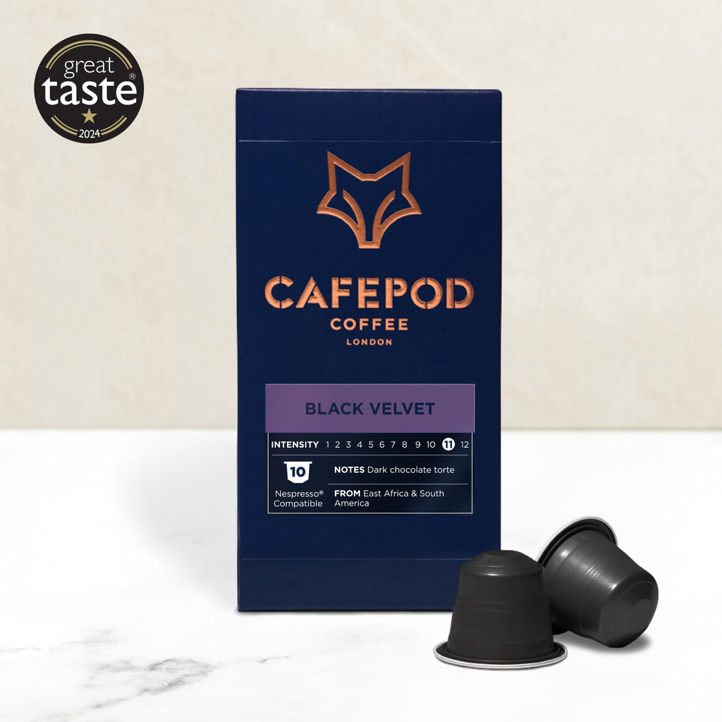 A box of CaféPod coffee pods with the flavor Black Velvet is displayed alongside two coffee pods. The box features the product name and description, with a graphic of a fox in orange at the top.