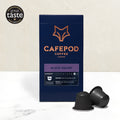 A box of CaféPod coffee pods with the flavor Black Velvet is displayed alongside two coffee pods. The box features the product name and description, with a graphic of a fox in orange at the top.