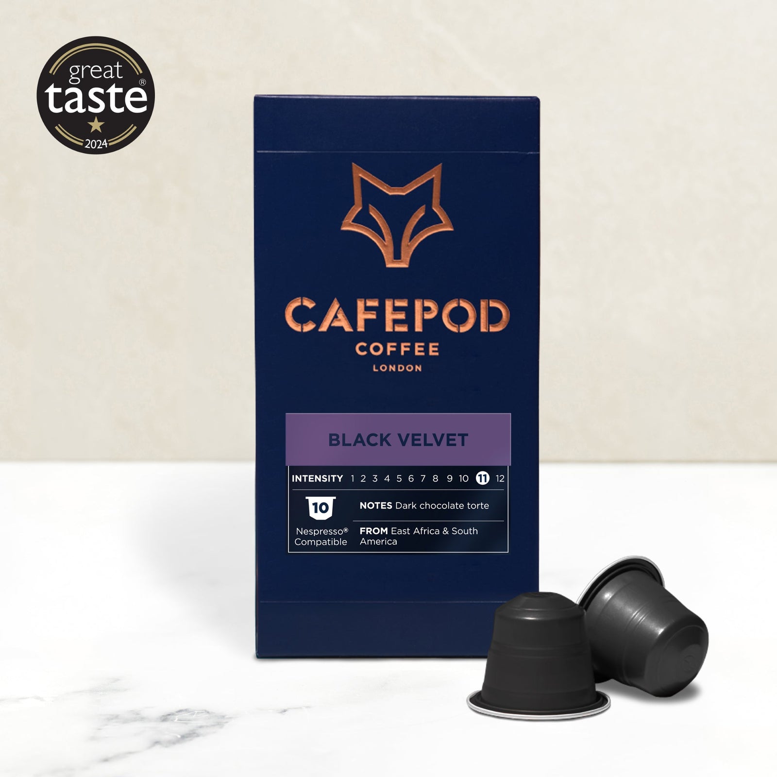 A box of CaféPod coffee pods with the flavor Black Velvet is displayed alongside two coffee pods. The box features the product name and description, with a graphic of a fox in orange at the top.