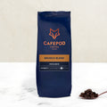 A navy blue bag of CaféPod Coffee branded Brunch Blend whole bean coffee, with a small scoop of coffee beans in front of the bag.