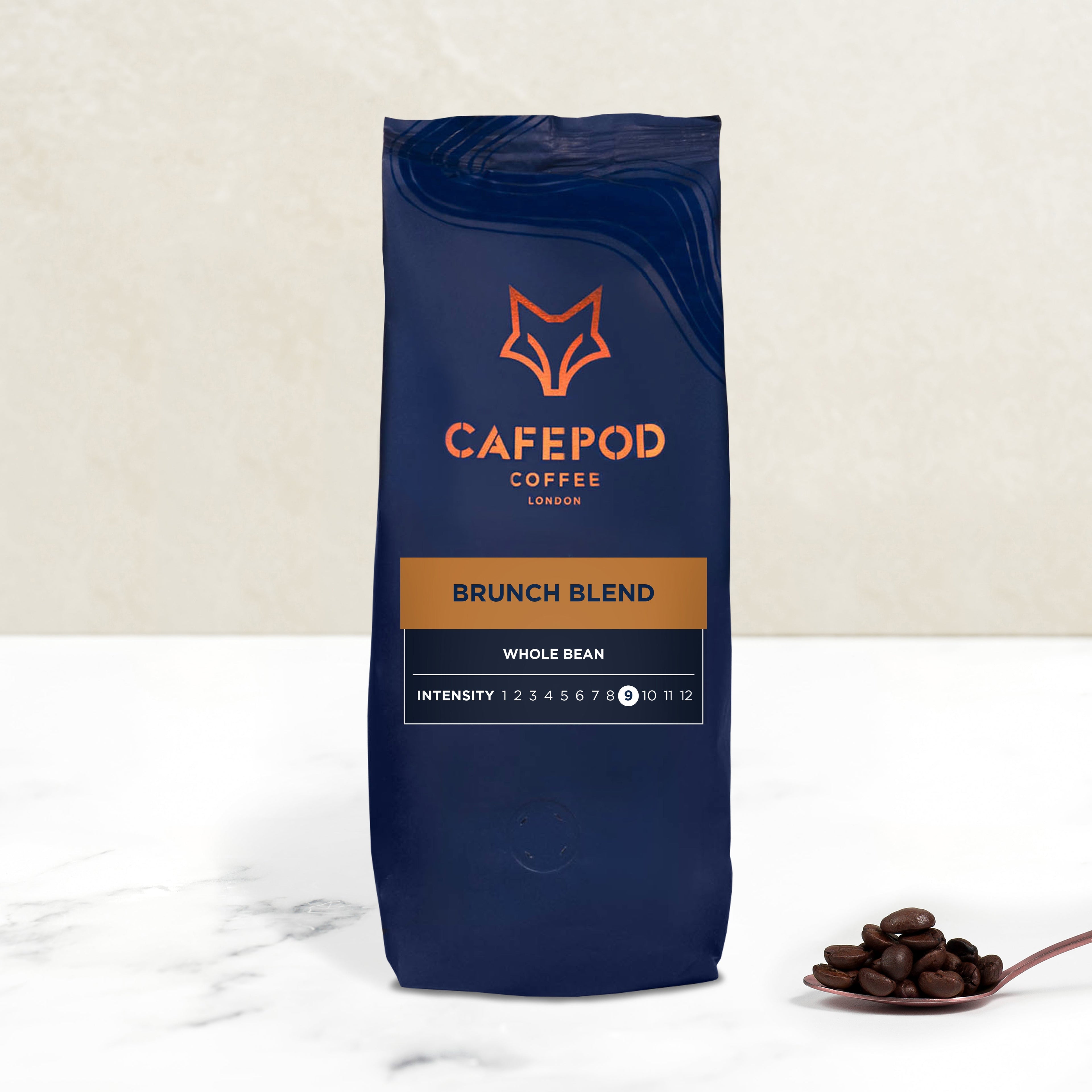 A navy blue bag of CaféPod Coffee branded Brunch Blend whole bean coffee, with a small scoop of coffee beans in front of the bag.