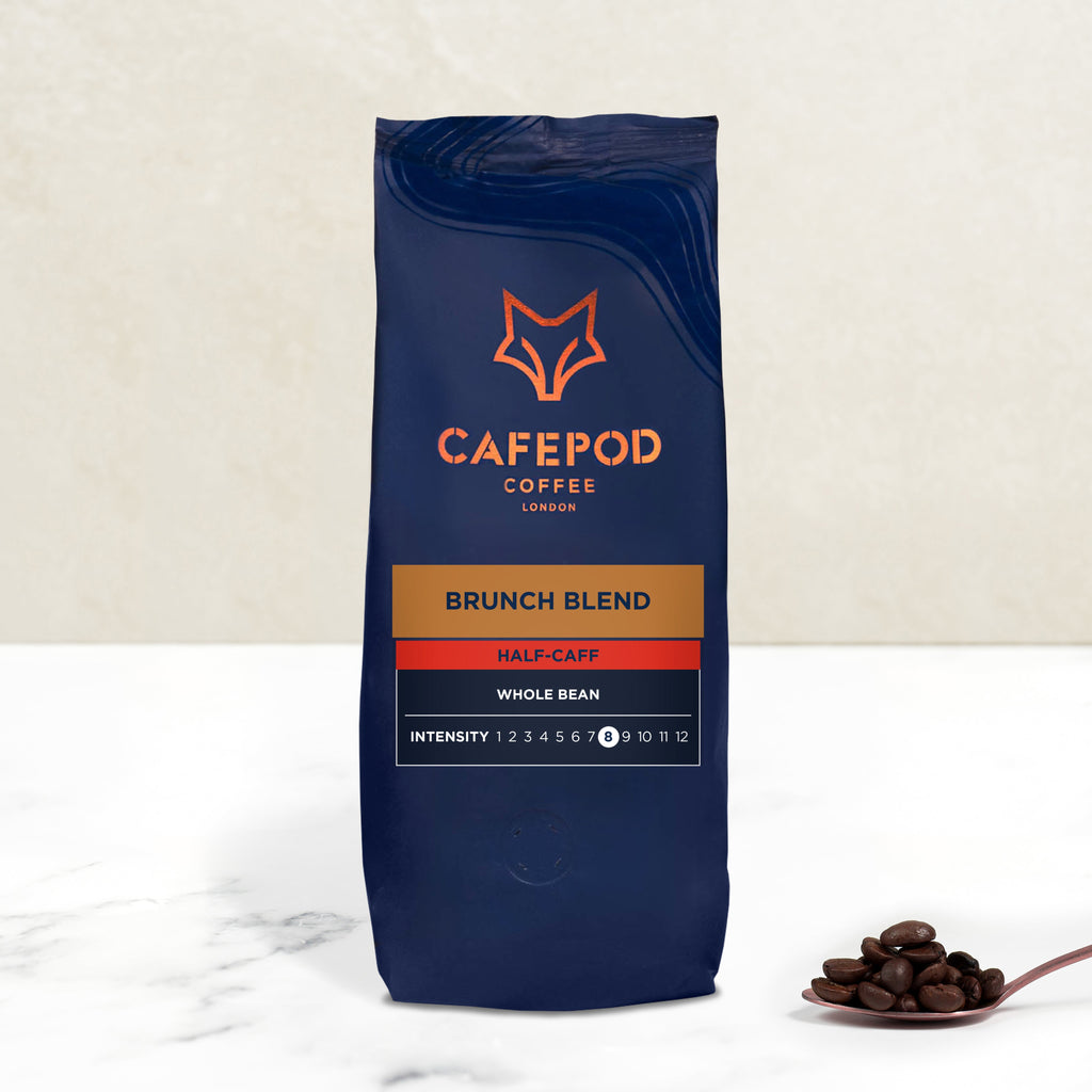A navy blue bag of CaféPod Coffee's Brunch Blend Whole Bean with a small scoop of coffee beans in front of it.