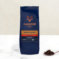 A navy blue bag of CaféPod Coffee's Brunch Blend Whole Bean with a small scoop of coffee beans in front of it.