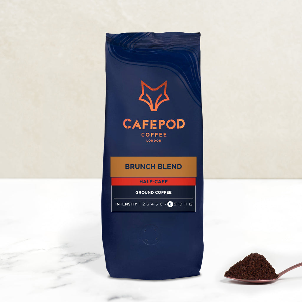 A navy blue bag of CaféPod Coffee's Brunch Blend Ground Coffee with a scoop of ground coffee in front, on a white background.