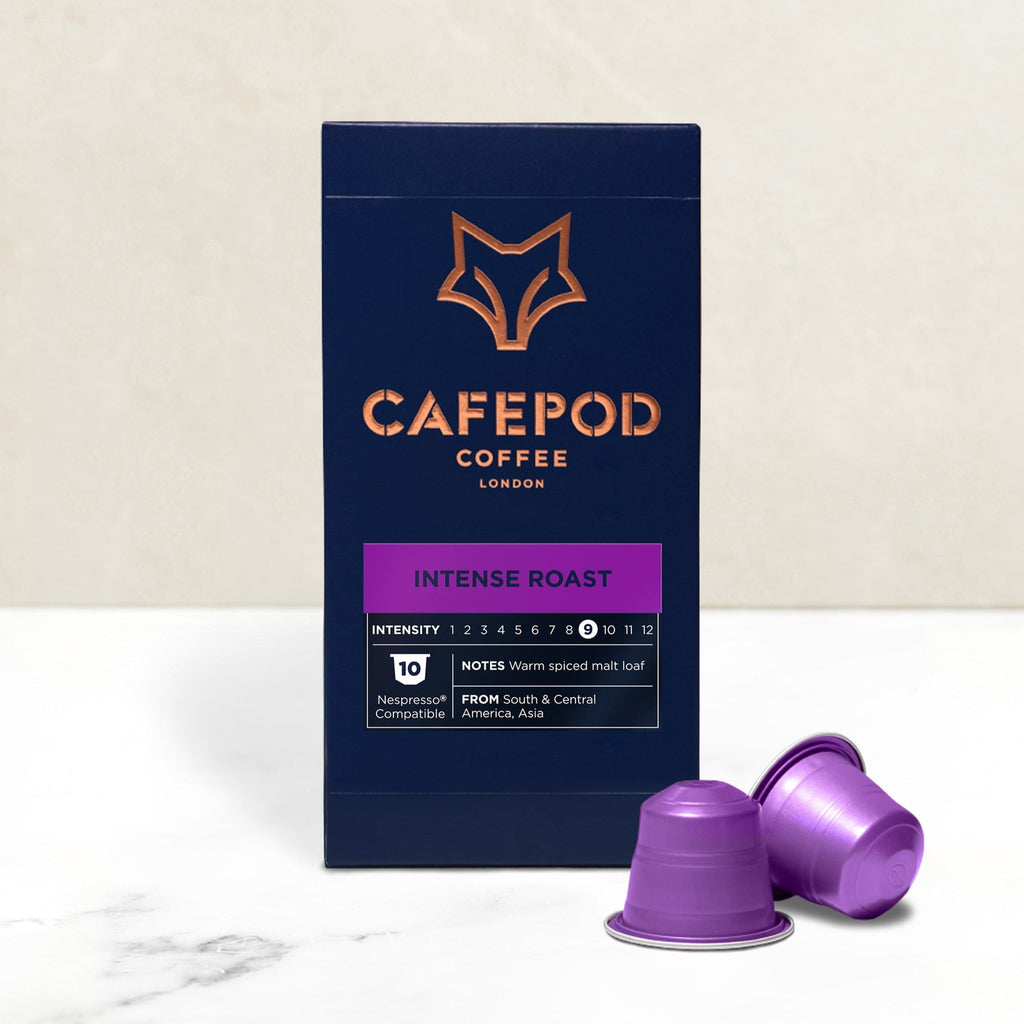 A box of CaféPod coffee capsules with the Intense Roast variety shown. Two purple capsules are displayed in front of the box, which has a graphic of a fox on it.