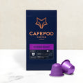 A box of CaféPod coffee capsules with the Intense Roast variety shown. Two purple capsules are displayed in front of the box, which has a graphic of a fox on it.