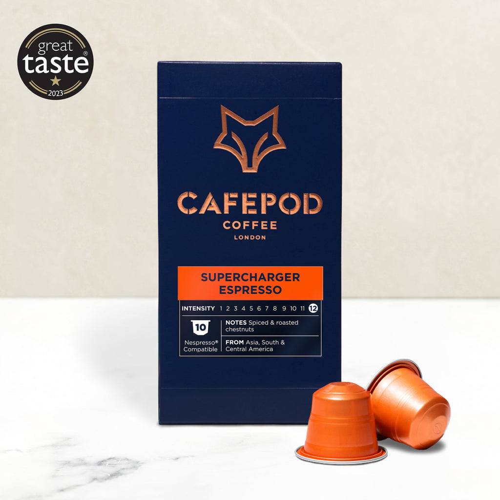 A box of CaféPod coffee pods with the name 'Supercharger Espresso' displayed on the front, alongside two orange coffee pods. The background is light-colored.