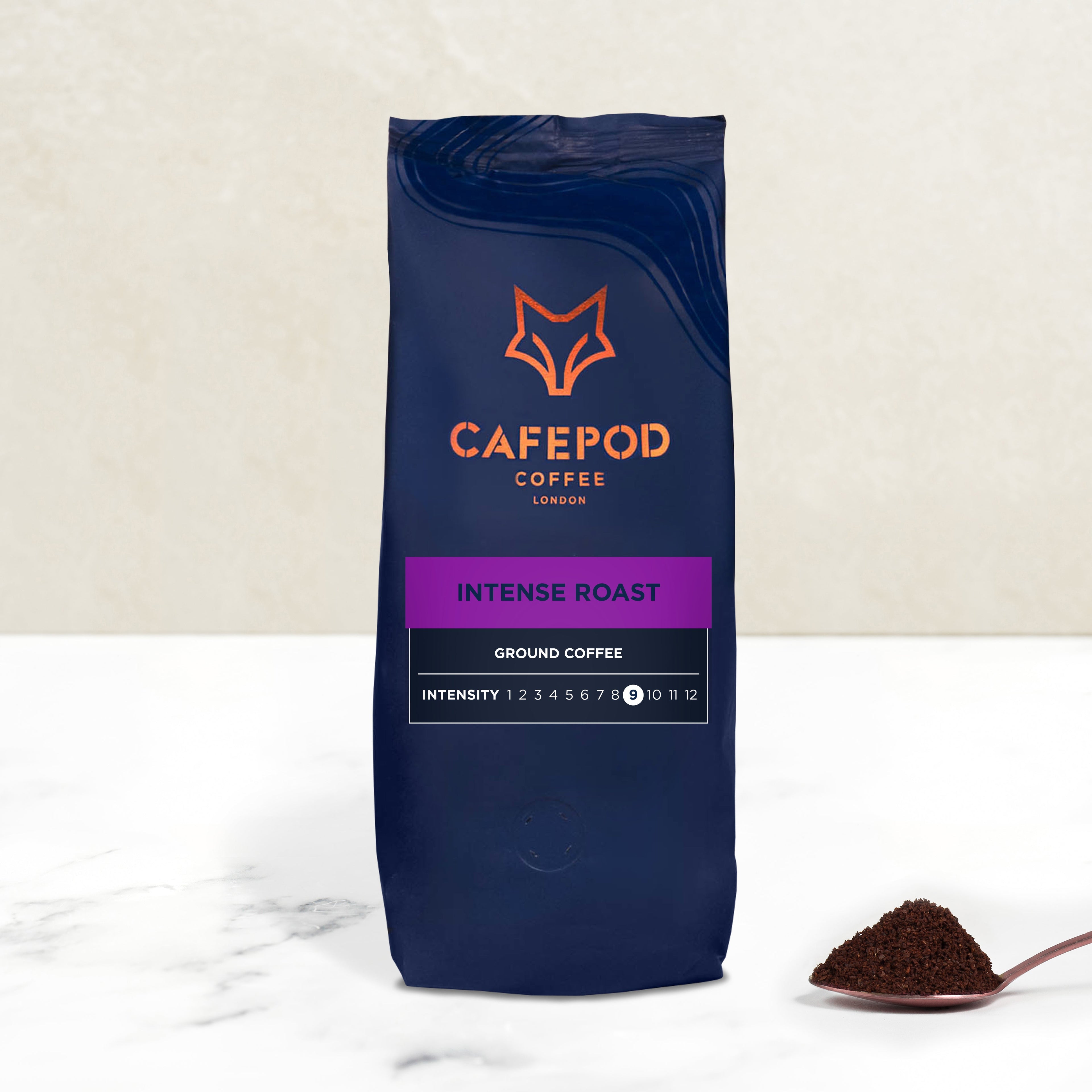 A navy blue bag of CaféPod coffee labeled 'Intense Roast Ground Coffee' with a scoop of ground coffee in front.