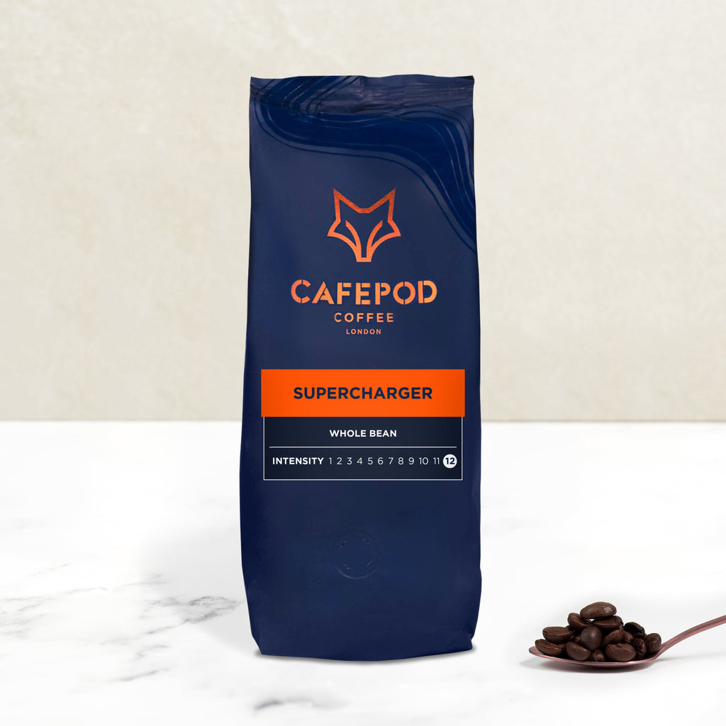A bag of Cafepod Supercharger whole bean coffee with a intensity rating, placed on a marble surface with a small amount of coffee beans scattered in front.