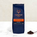 A bag of Cafepod Supercharger whole bean coffee with a intensity rating, placed on a marble surface with a small amount of coffee beans scattered in front.