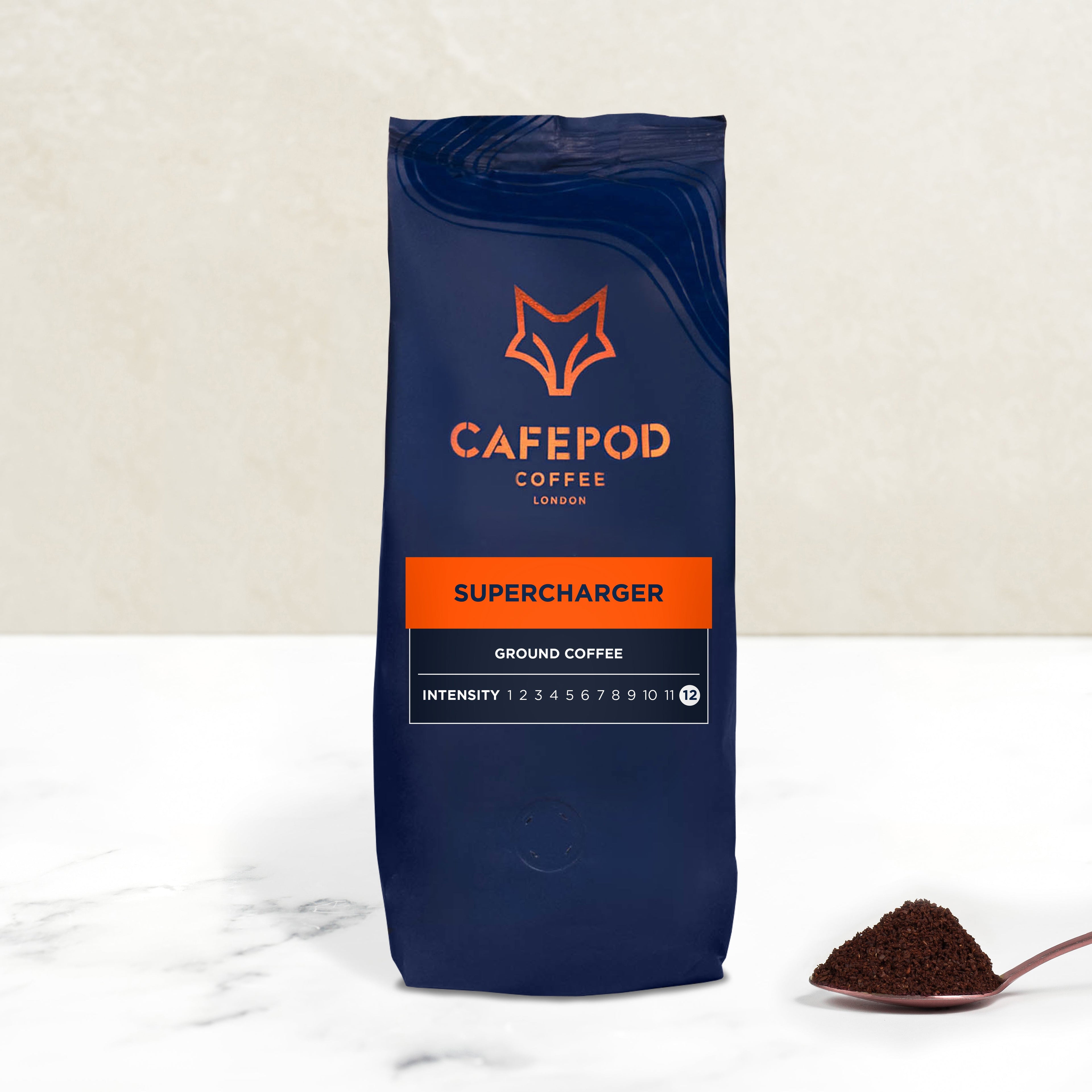 A bag ofCAFEPOD Supercharger ground coffee with a scoop of coffee grounds in front of it on a marble surface.