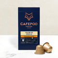 A box of CaféPod coffee pods with the flavor 'You're So Vanilla' displayed alongside two coffee pods. The box features the CaféPod logo and branding in gold and orange colors.